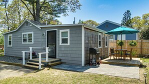 A small, single-story house with a front porch, a patio with outdoor furniture, and a wooden fence. - Periwinkle: Gateway to Cape Cod Coastal Cottage (Wareham)