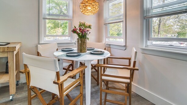 A dining area with a round table, white chairs, a hanging light fixture, and a vase with flowers. - Periwinkle: Gateway to Cape Cod Coastal Cottage (Wareham)