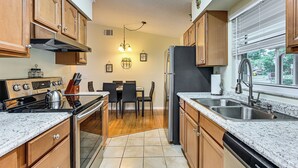 A kitchen with wooden cabinets, a stove, a refrigerator, and a dining area with chairs and a table. - Walk to Lake Ariana Park! Home w/ Screened Porch (Auburndale)