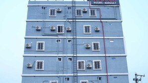 Een hotel met meerdere verdiepingen, voorzien van airconditioners, een bord met 'NSK Grand Rooms - Banquet' en een zichtbare ladder aan de buitenkant.