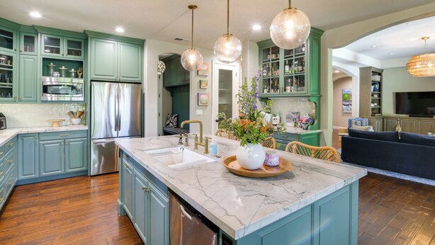 Une cuisine spacieuse dotée d’un îlot en marbre, d’appareils électroménagers en acier inoxydable et de meubles de couleur turquoise.