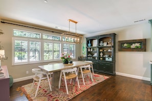 A dining area with a table, chairs, a rug, and a window with blinds.