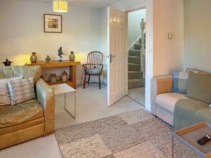 Ein Wohnzimmer mit einer Couch, einem Sessel, einem kleinen Tisch, einem Teppich, einer Treppe und einer Tür zu einem anderen Raum.