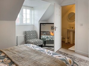 Ein Schlafzimmer mit Bett, Sessel, Fenster und offener Tür zu einem Badezimmer.