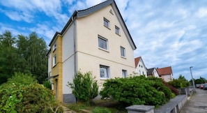 A multi-story residential building with a sloped roof, surrounded by greenery and a paved pathway. - Quiet and Cozy Ground Floor Apartment with Balcony and Wi-Fi (Herford)