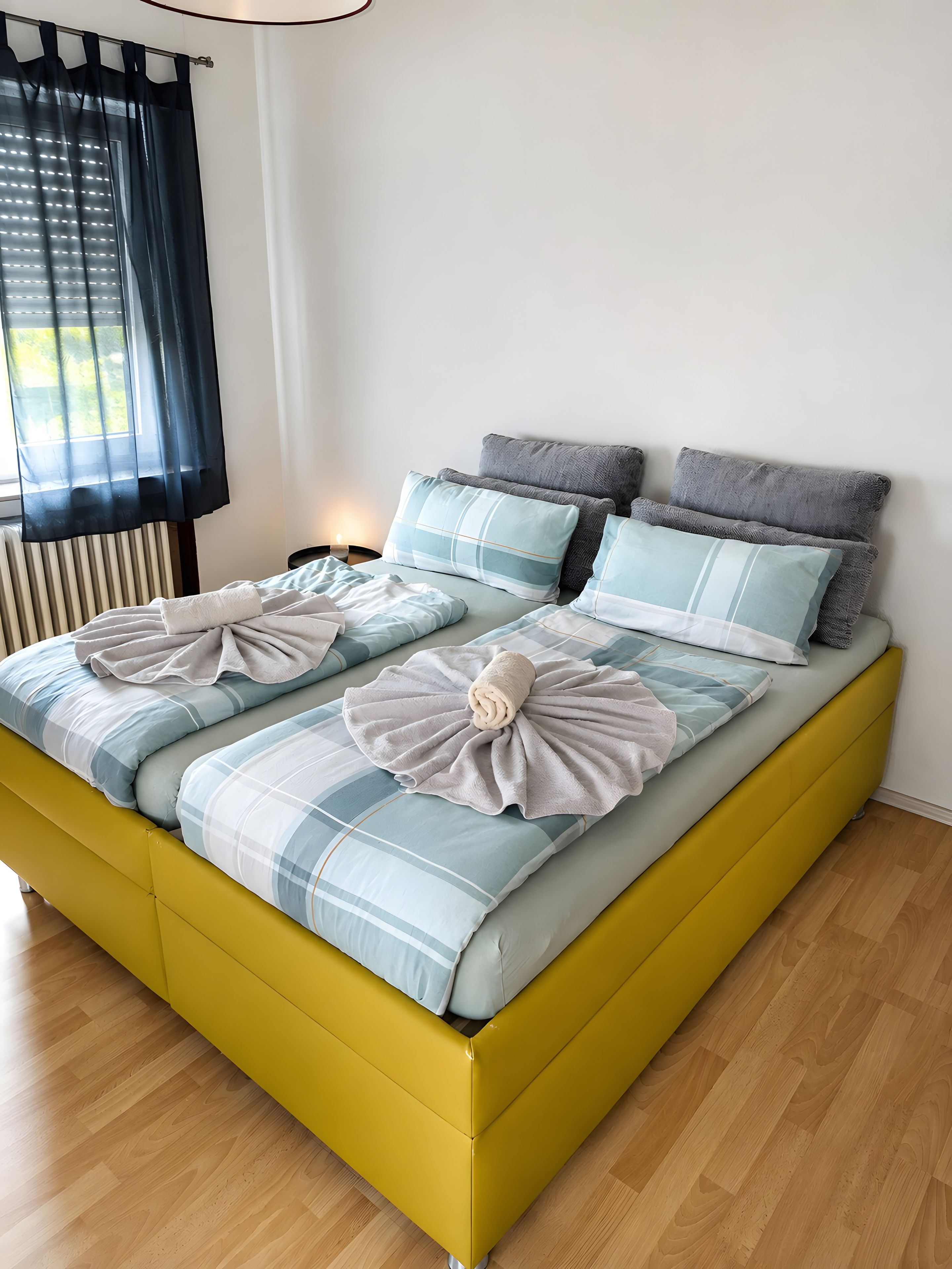A bed with a yellow frame, blue and white bedding, and a towel decoration.
