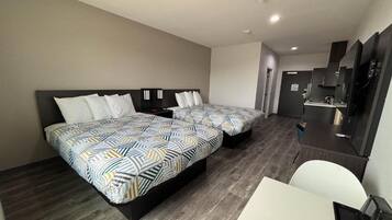 A hotel room with two beds, a desk, a chair, and a kitchenette.