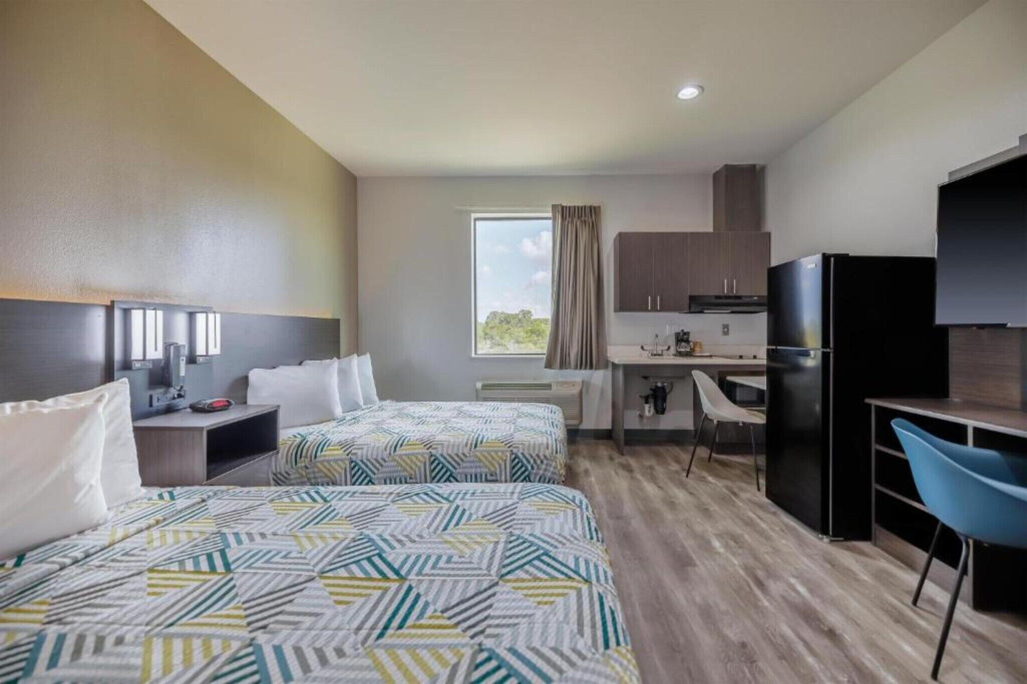 Een hotelkamer met twee bedden, een kitchenette, een bureau en een stoel.