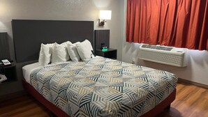 Ein Hotelzimmer mit Bett, Nachttisch, Lampe, Heizung und einem Fenster mit Vorhängen.