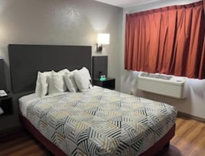 A hotel room with a bed, a nightstand, a lamp, a window with curtains, and a radiator.