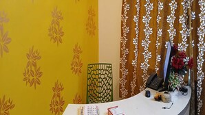 A reception desk with a yellow patterned wall, a green chair, a telephone, a computer monitor, and a vase with red flowers. - Hotel O Park Street Metro Station (Kolkata)