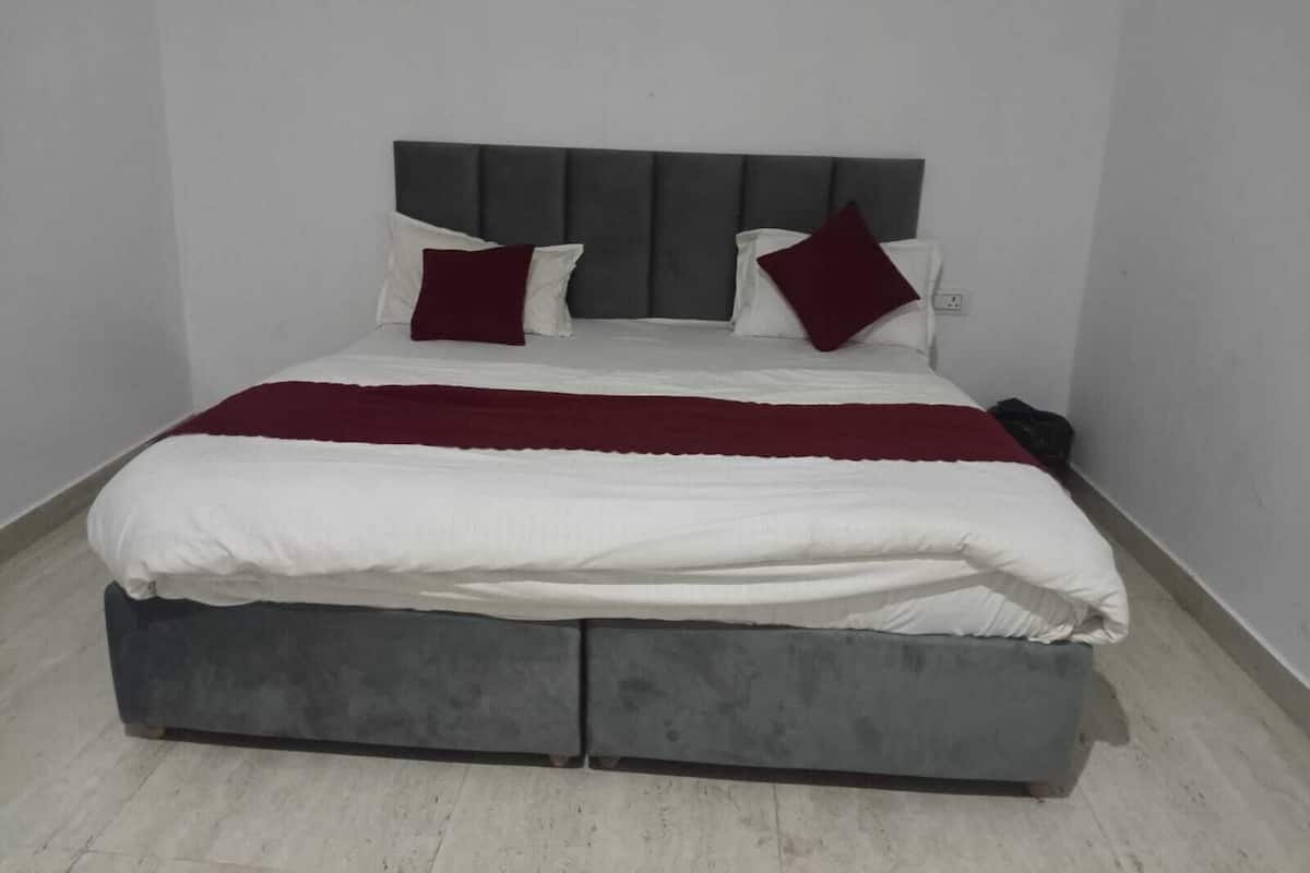 A bed with a grey headboard, white bedding, and two red pillows.