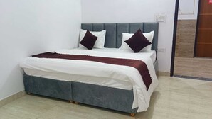 A bed with a grey headboard, white bedding, and two dark pillows. - HR Residency (New Delhi)