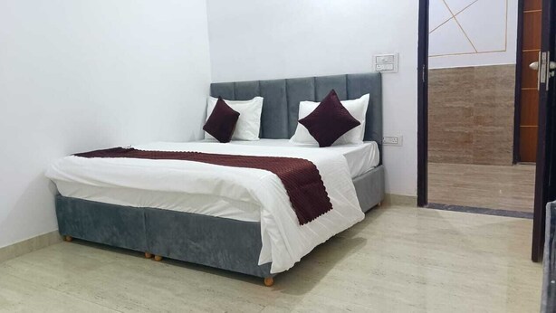 A bed with a grey headboard, white bedding, and two dark pillows. - HR Residency (New Delhi)