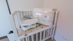 Ein Teil eines Raumes mit einem weißen Babybett, einer weißen Wickelkommode und einer weißen Wand.