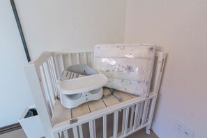 Ein Teil eines Raumes mit einem weißen Babybett, einer weißen Wickelkommode und einer weißen Wand.
