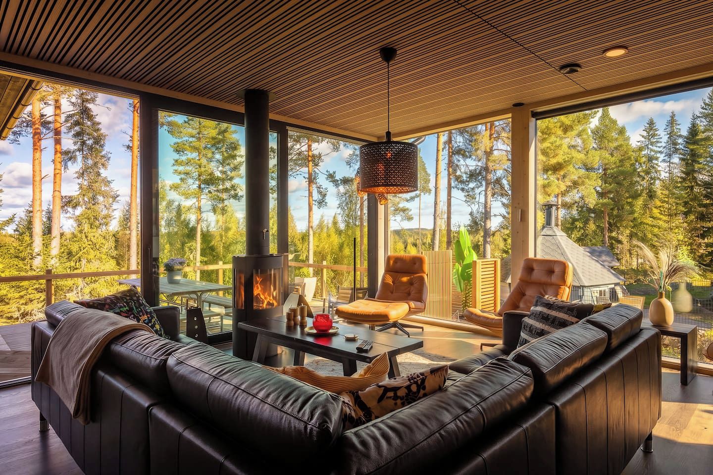 Una sala de estar moderna con un sofá grande, una chimenea y vistas a un bosque.