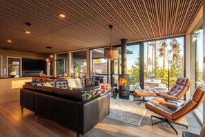 A modern living room with a large black leather sofa, a fireplace, and a dining area with a TV.