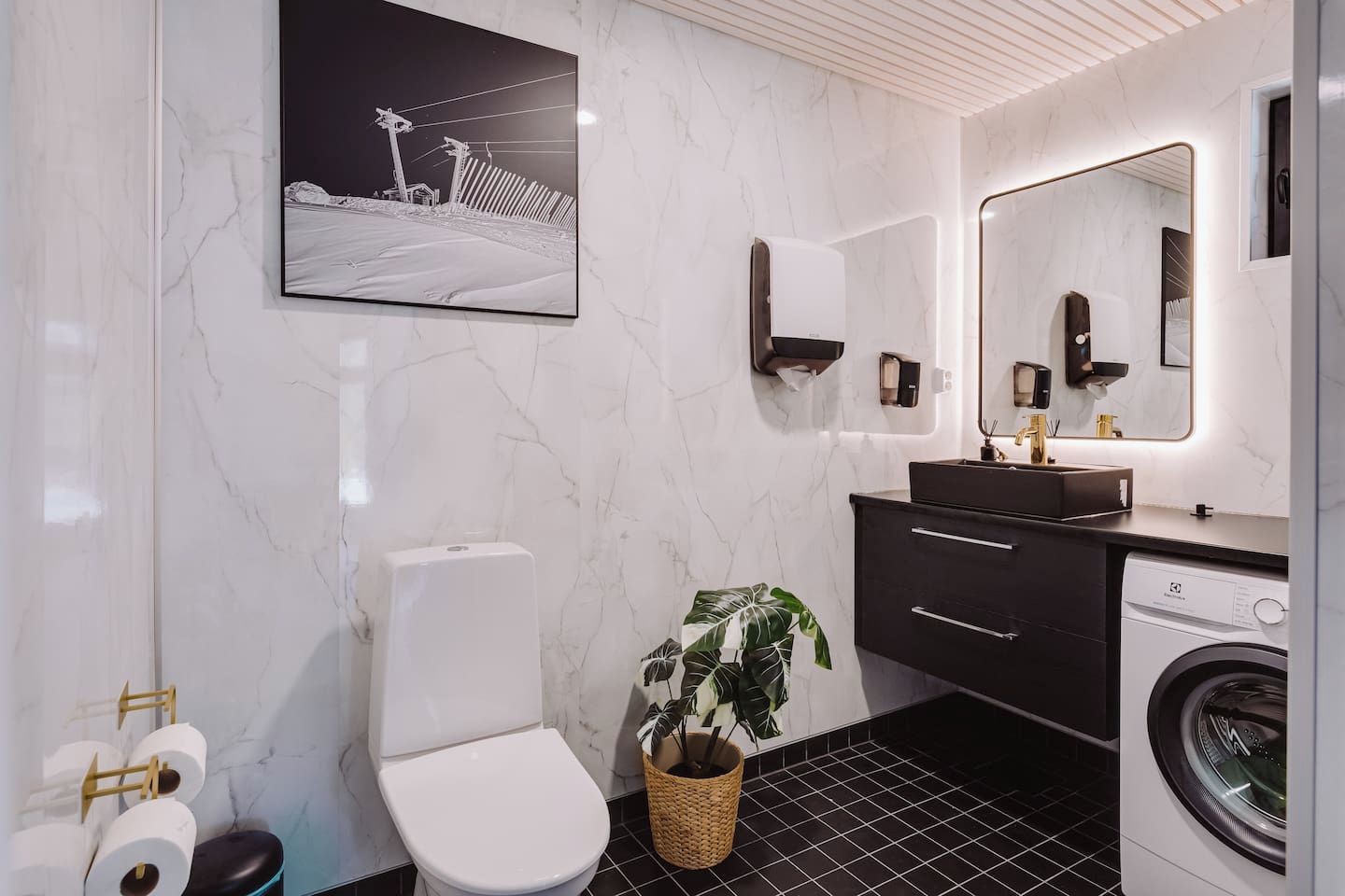A modern bathroom with a toilet, sink, mirror, and washing machine.