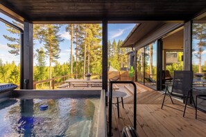 A wooden deck with a hot tub, outdoor seating, and a view of a forest.