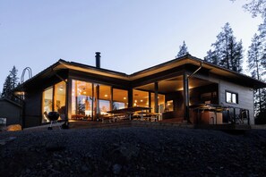 A modern house with large glass windows, a covered outdoor seating area, and a chimney.