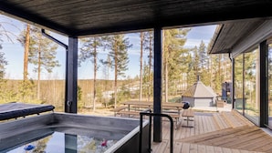 Ett takförsett utomhusområde med en bubbelpool, ett trädäck, picknickbord och utsikt över ett skogsområde.