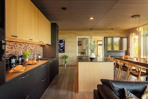 Une cuisine moderne avec des meubles de couleur sombre, un îlot central en bois et un coin repas agrémenté d’un canapé en cuir noir.
