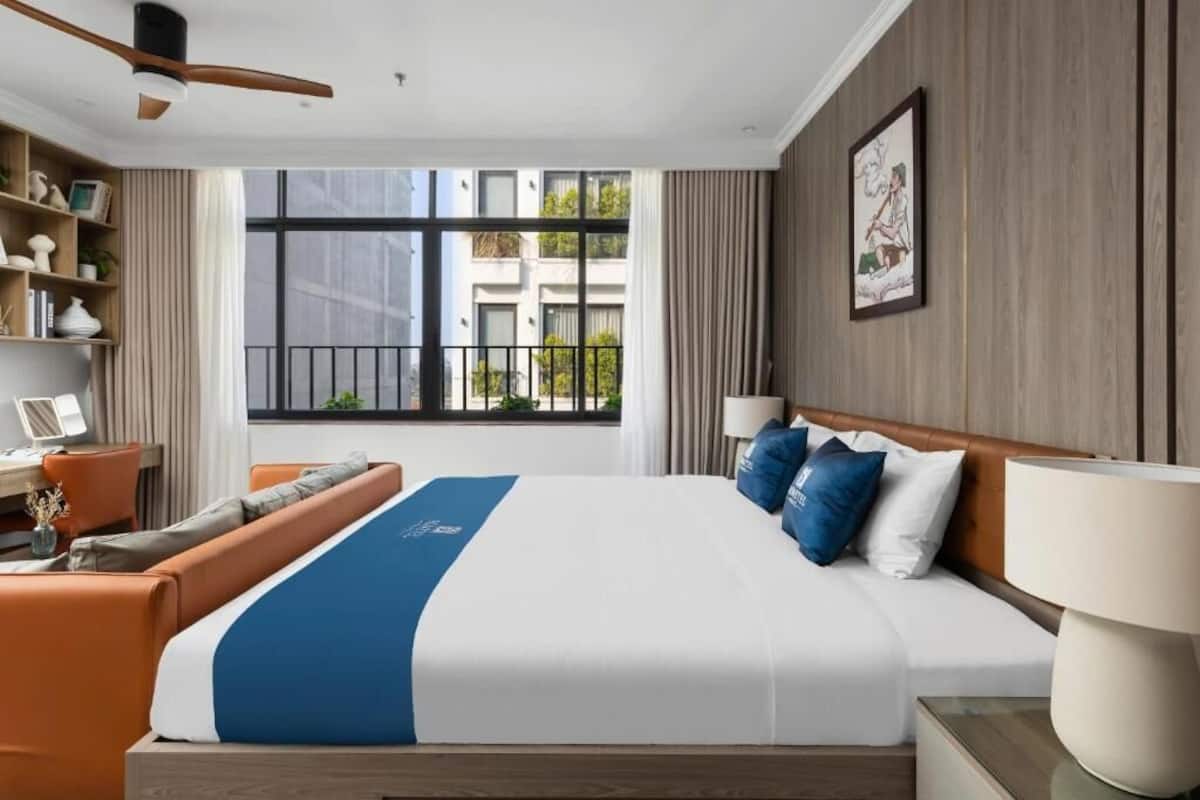 A hotel room with a large bed, a desk, a chair, and a view of buildings outside.