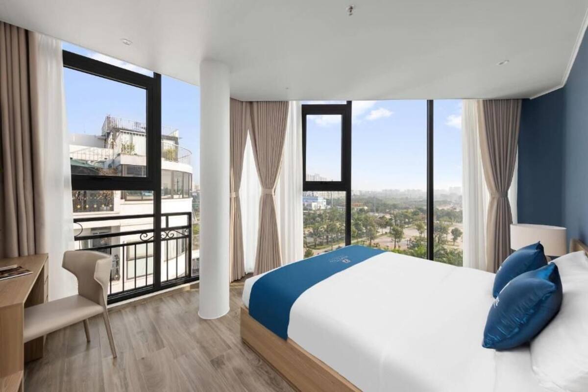 A modern hotel room with a large bed, a desk, and a balcony with a city view.