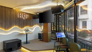 A modern interior with a 'HOP Coffee & Music' sign, a flat-screen TV, a digital menu board, and a seating area with chairs and a table. - 3A Hometel Hanoi (Hanoi)