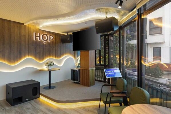 Un interior moderno con un letrero de 'HOP Coffee & Music', un televisor de pantalla plana, un menú digital y una zona de estar con sillas y una mesa.