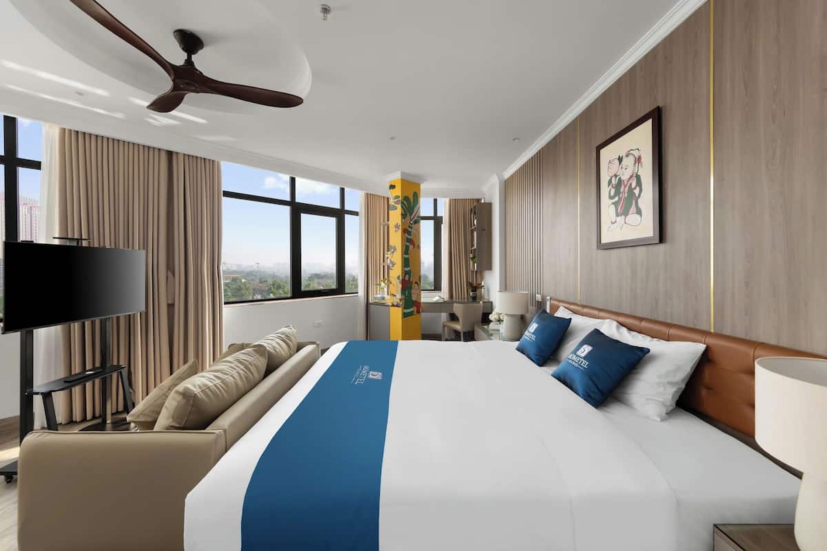A hotel room with a large bed, a TV, a sofa, and a desk.