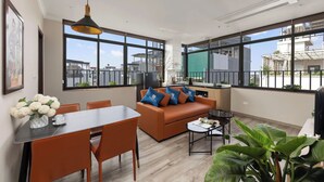 A modern living room with a sofa, dining table, and chairs, large windows, and a hanging light fixture. - 3A Hometel Hanoi (Hanoi)