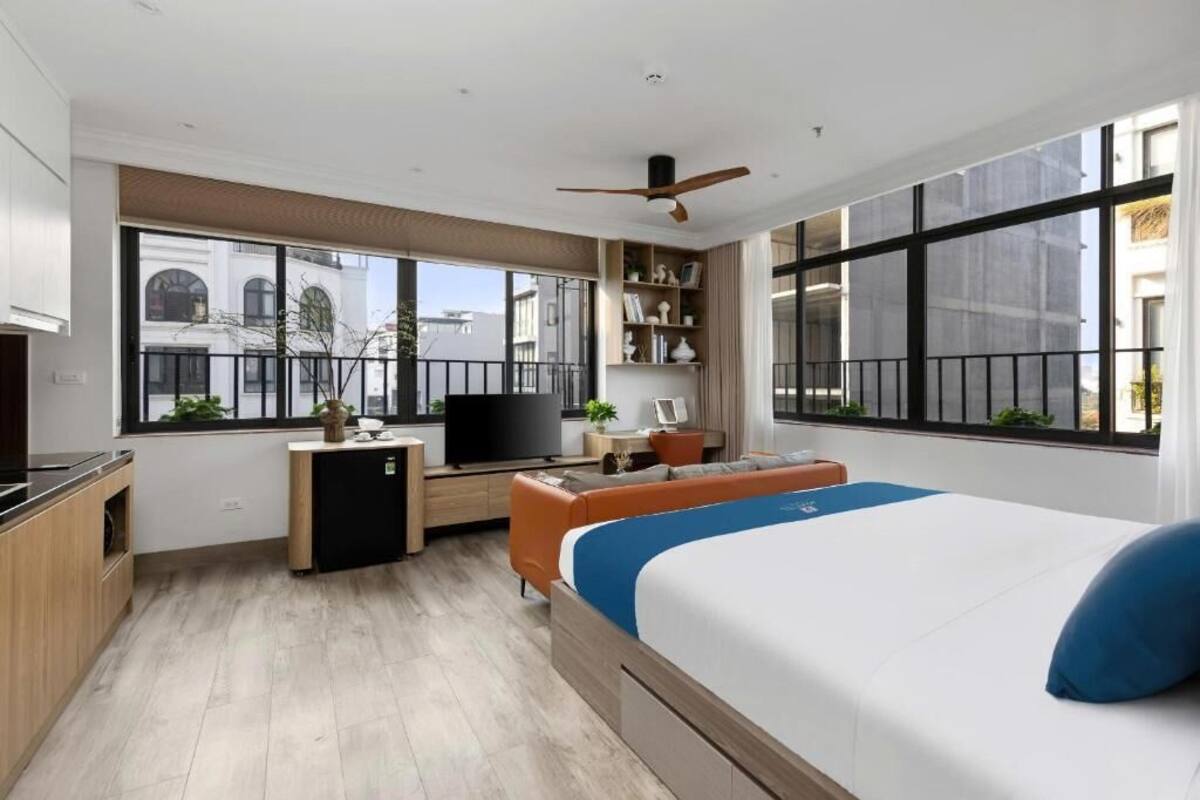 A modern hotel room with a bed, desk, television, and large windows.