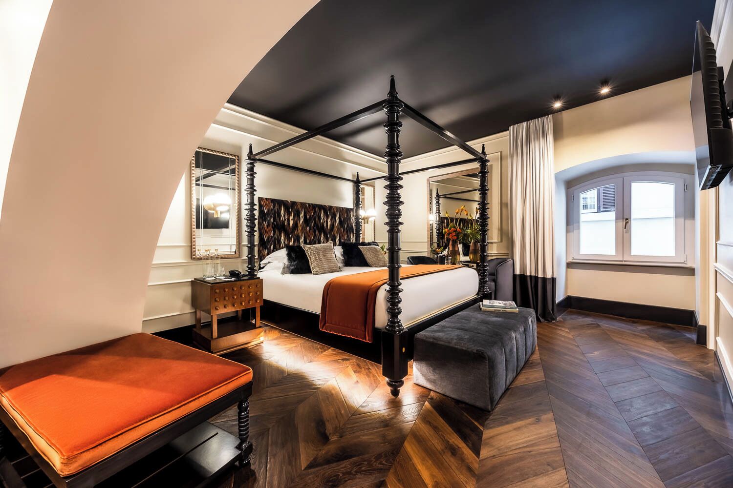 Una cama con dosel en un dormitorio moderno con un ventanal grande, una mesita de noche y un banco.