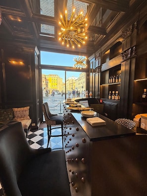 A bar area with a view of a city square, a chandelier, and a bar stocked with bottles. - Argentum Boutique Hotel & SPA (Rome)