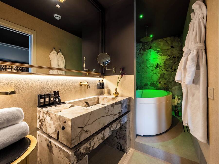 Un baño moderno con lavamanos de mármol, un espejo grande, una pared iluminada en verde y una bañera.