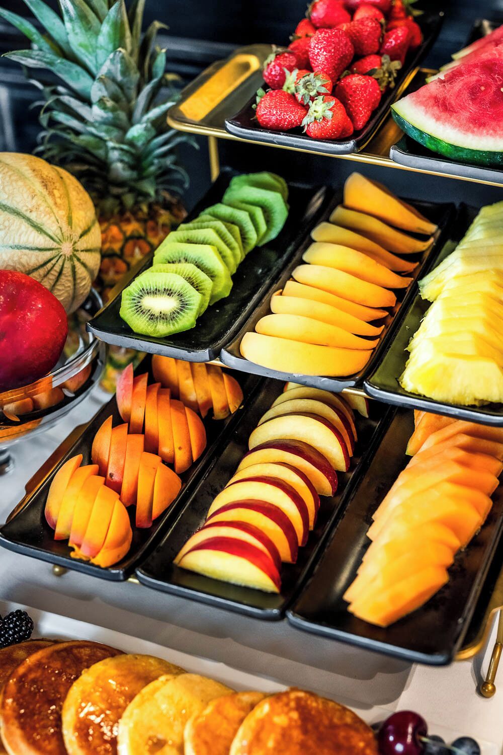 A buffet with various fruits and sliced apples arranged on trays.