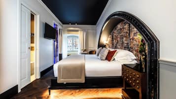 Un dormitorio con una cama grande, televisor y vista a edificios a través de una ventana.