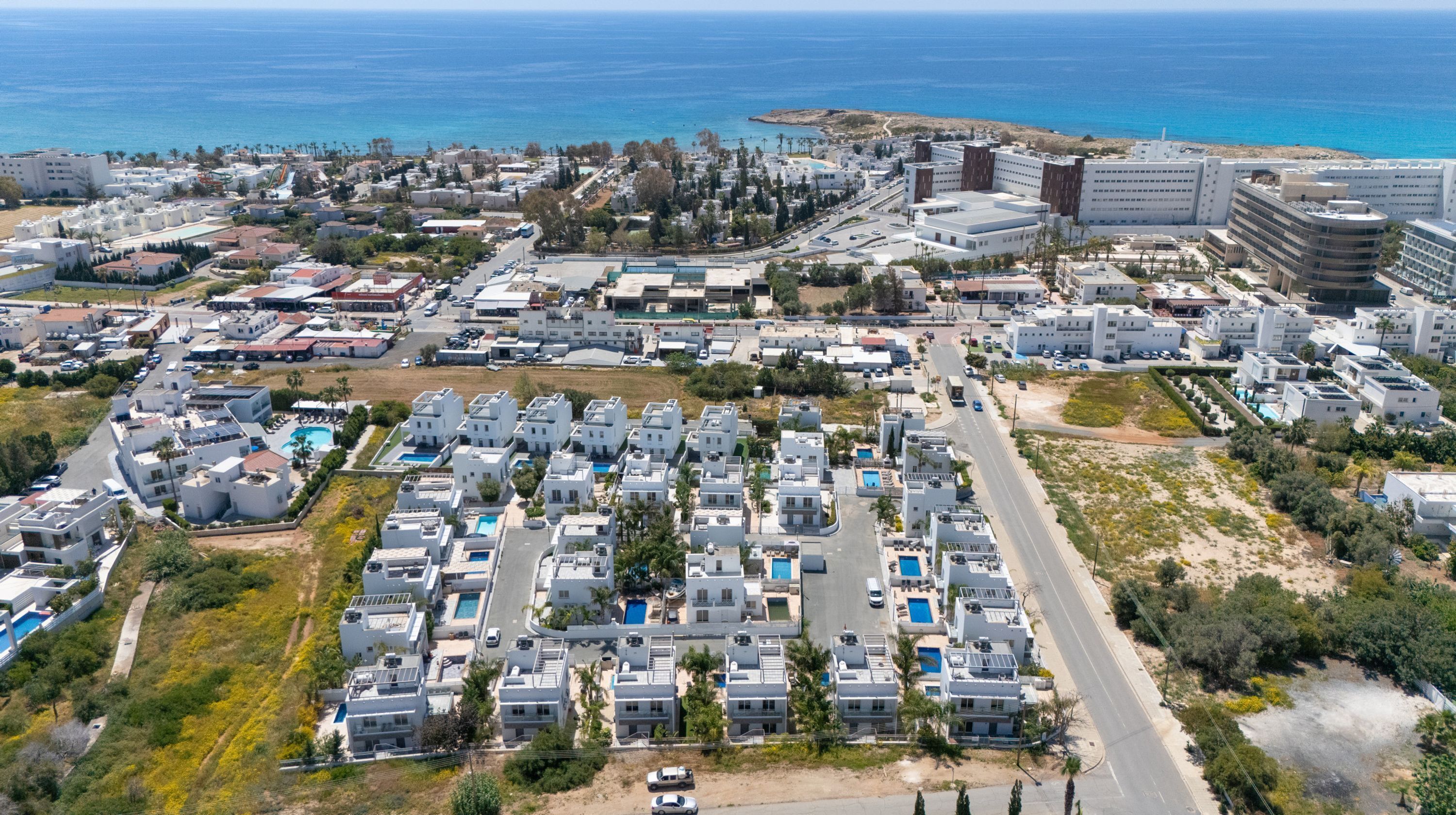 Vista aérea de una zona residencial costera con edificios modernos, una avenida principal y una playa al fondo.