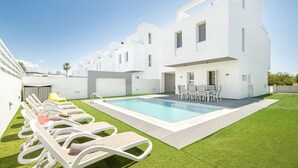 En modern vit byggnad med en swimmingpool, solstolar och en liten uteplats.