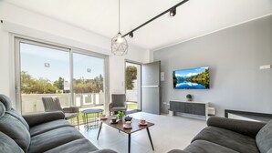 Ett modernt vardagsrum med en soffa, ett bord med dekorativa föremål, en tv och en skjutdörr i glas som leder ut till ett utomhusområde.