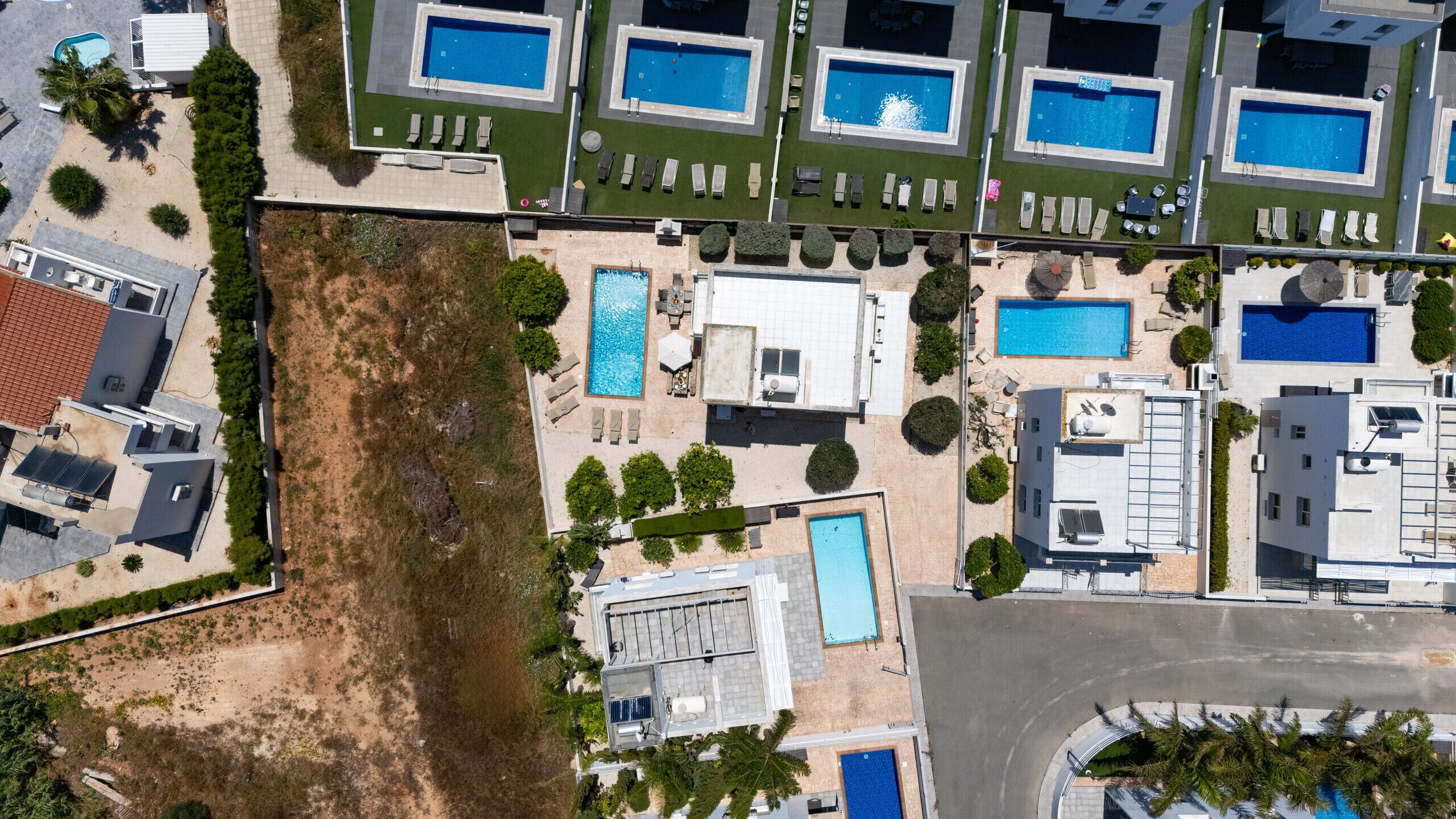 Vista aérea de un complejo turístico con múltiples piscinas, tumbonas y un edificio grande de techo plano.