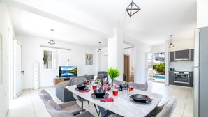 A modern dining area with a large table, grey upholstered chairs, and a view of the outdoors. - Nissini Villa 15 in Ayia Napa (Ayia Napa)