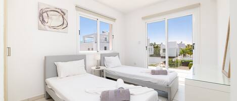 A modern hotel room with two beds, a glass door leading to a balcony, and a view of the cityscape.