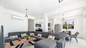 A modern living room with a sectional sofa, a wooden coffee table, and a dining area with chairs. - Nissini Villa 15 in Ayia Napa (Ayia Napa)
