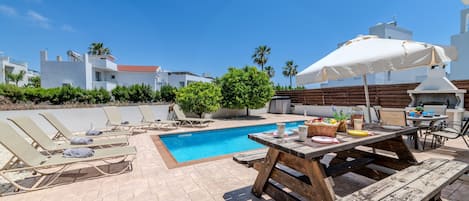 A poolside area with lounge chairs, a picnic table, and umbrellas.