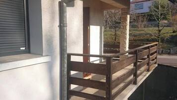 Un balcon doté d’une balustrade en bois, d’un mur en béton et d’une fenêtre avec des stores.