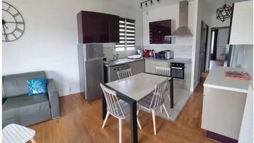 Une cuisine compacte avec un coin repas, un canapé gris et une horloge au mur.