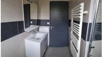 Une petite salle de bain avec un lavabo blanc, un miroir et une porte.